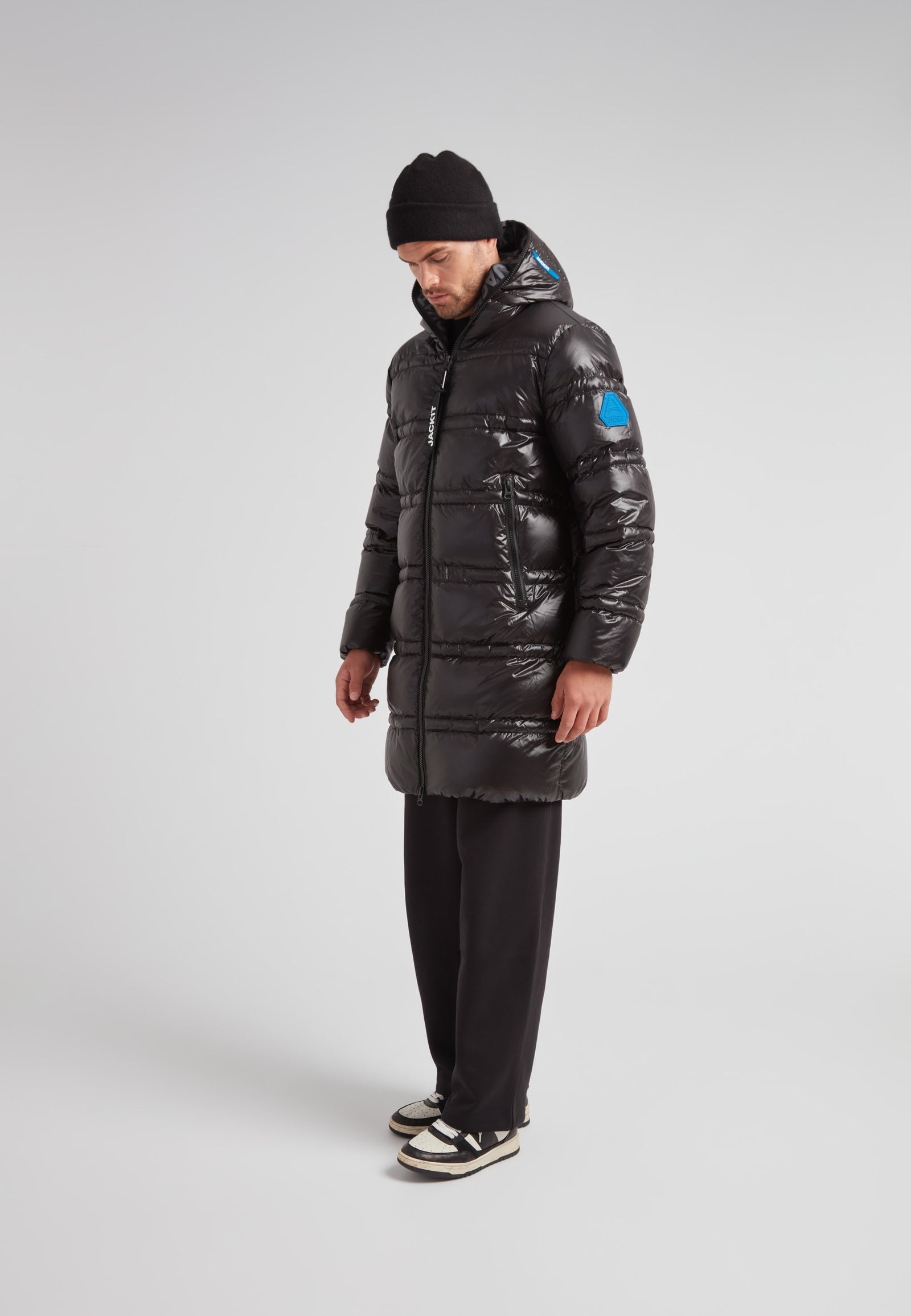 R4D Tramline Puffer Coat Lux Black worn by a man standing in profile, showcasing its longline design and insulation.