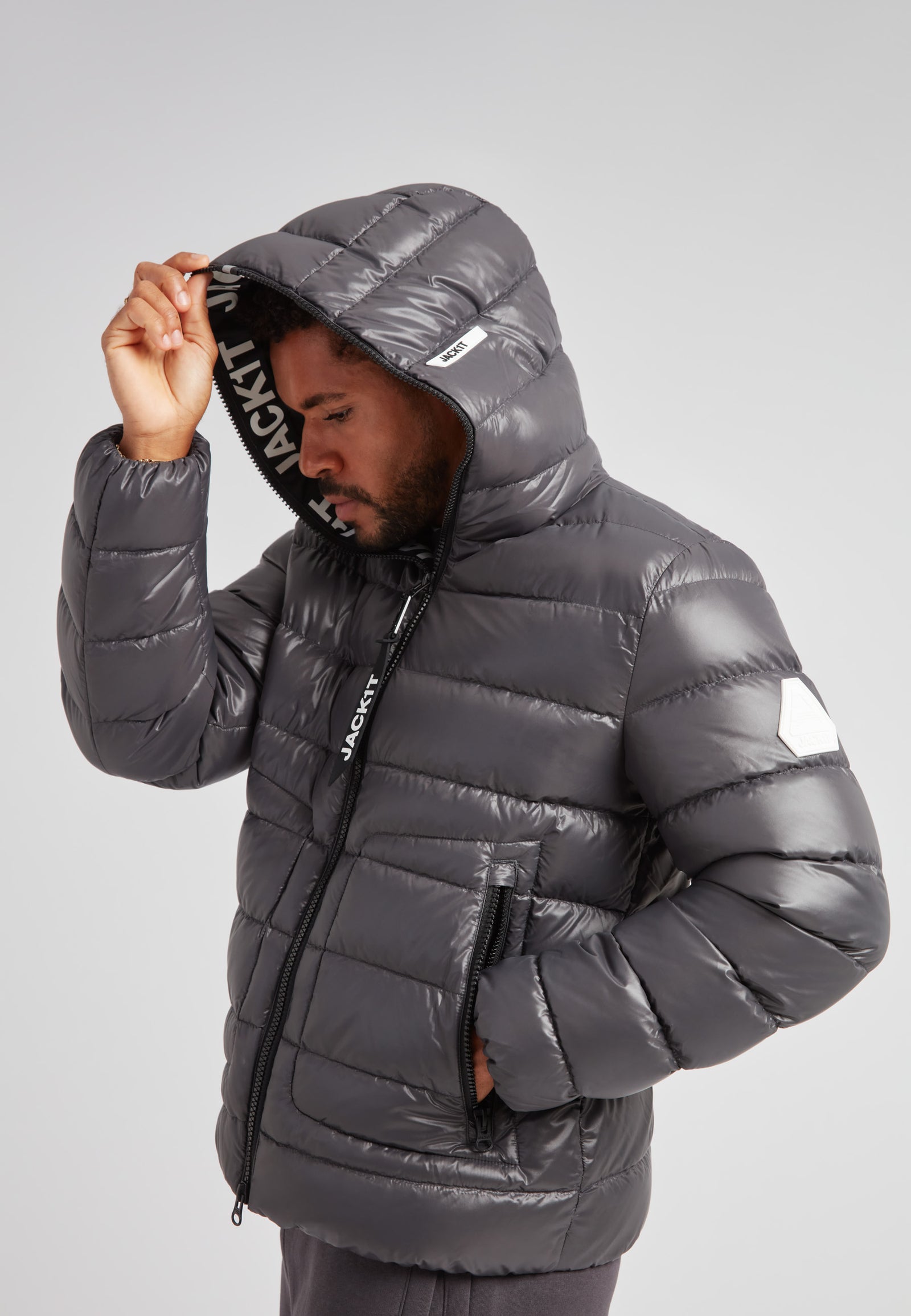 Model wearing the R4D Tramline Puffer Racer Jacket Lux Graphite with hood up, showcasing a sleek design.