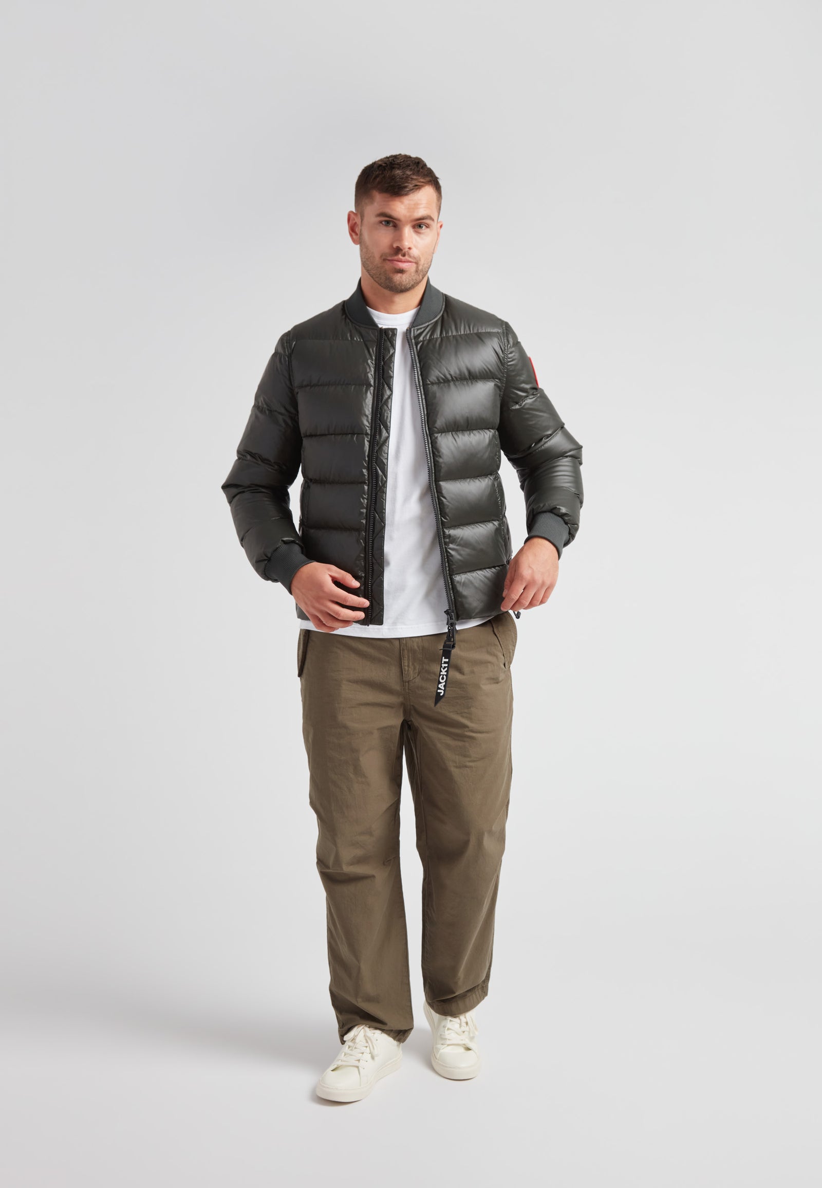 A model wearing a Vortex olive bomber jacket paired with olive trousers and a white t-shirt against a plain background.
