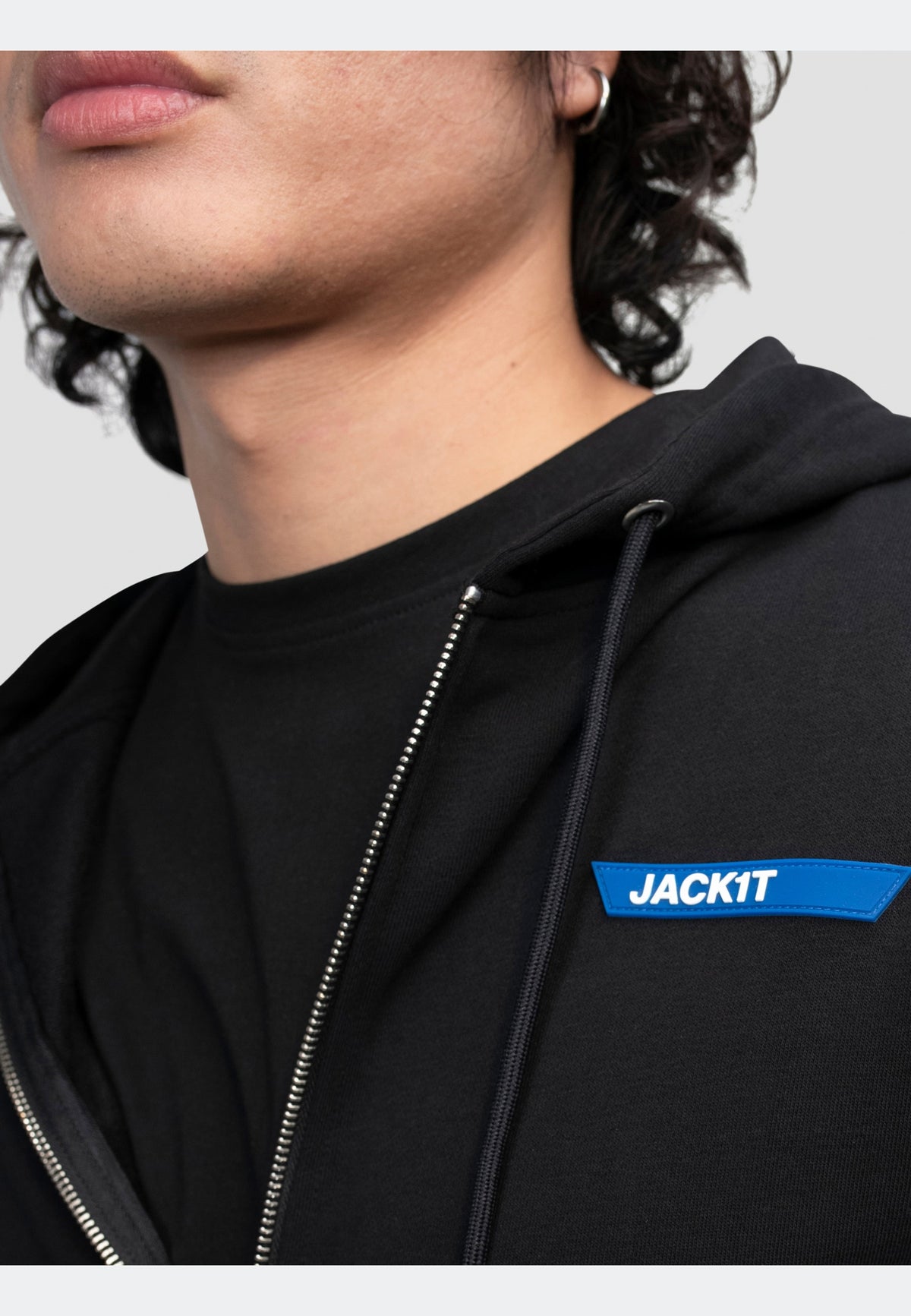 Close-up of a model wearing a black hoodie with a full zip and brand detailing, showcasing relaxed comfort.
