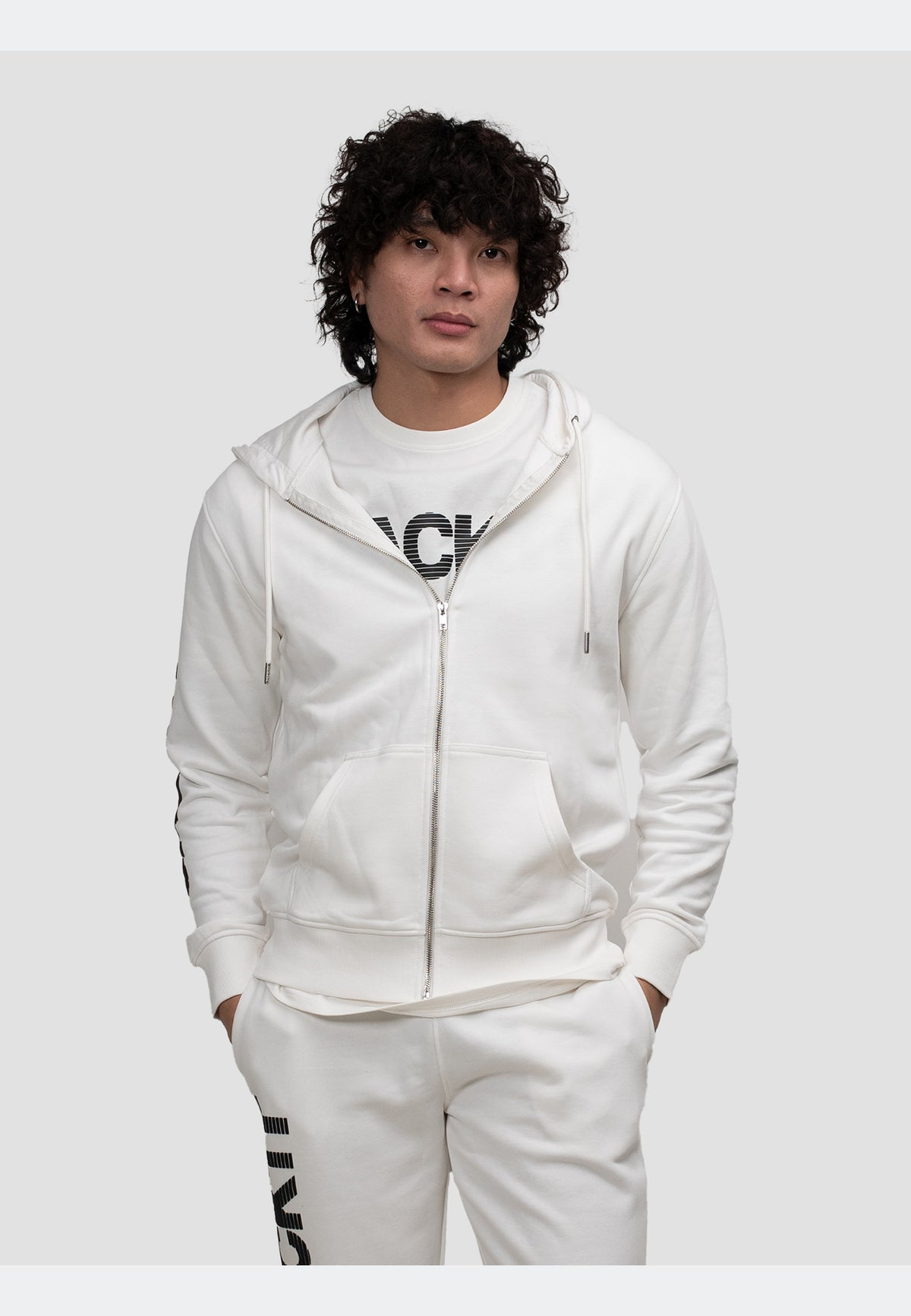 Model wearing an off white zip-through hoodie, styled with matching off-white pants and a graphic t-shirt.
