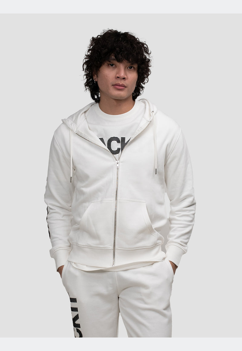 Model wearing an off white zip-through hoodie, styled with matching off-white pants and a graphic t-shirt.