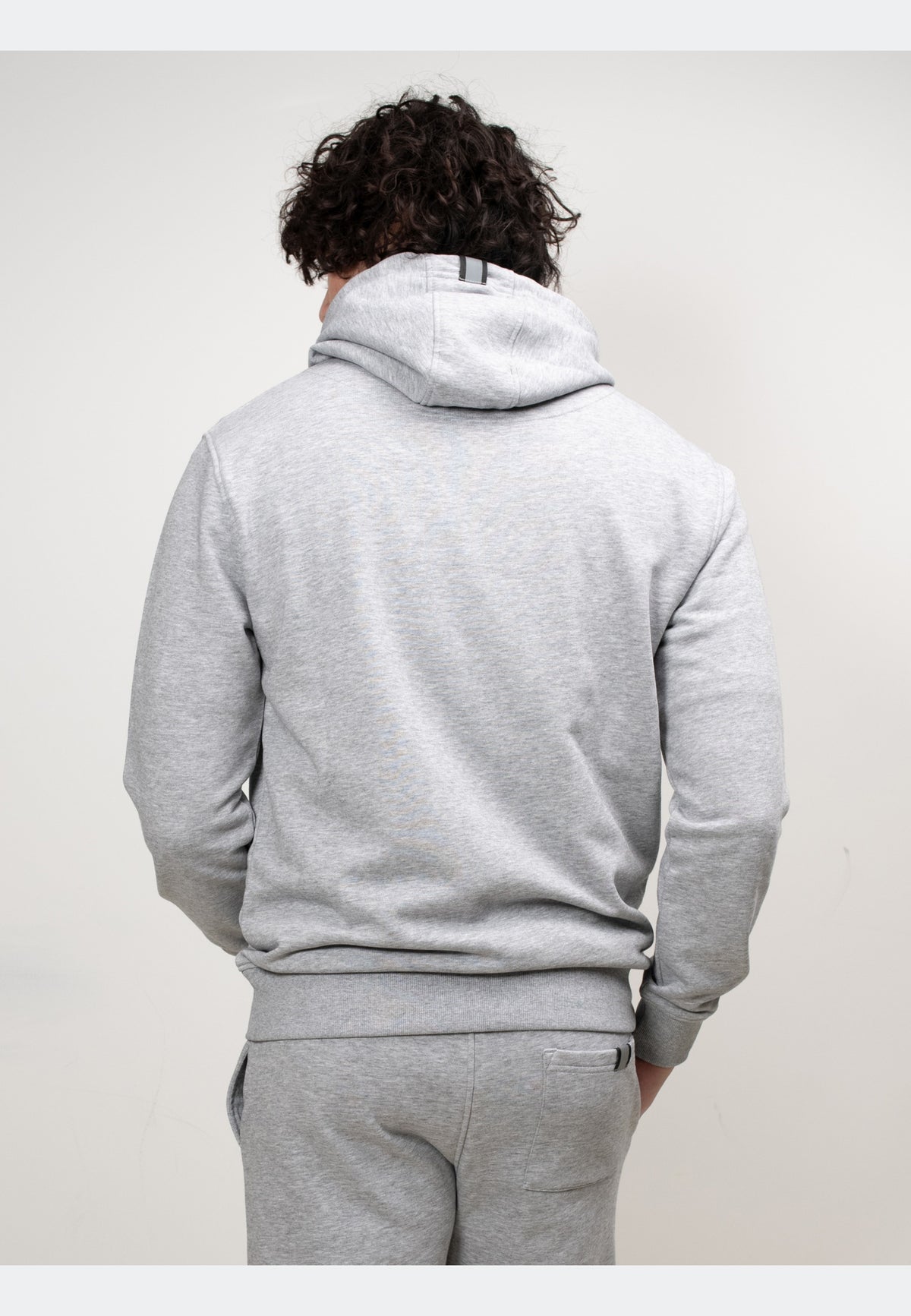 Back view of a model wearing a grey hoodie, showcasing its relaxed fit and hood design.