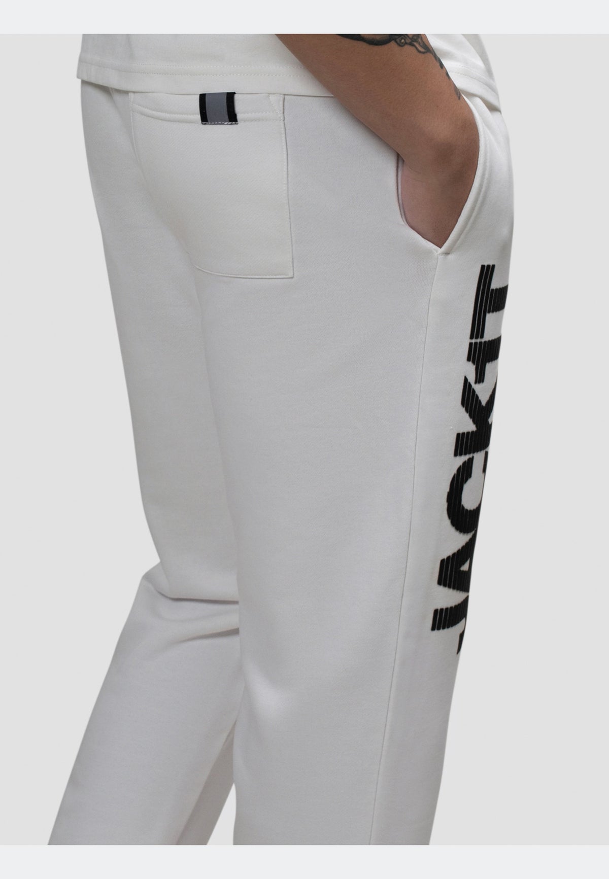 Side view of off white joggers featuring pockets and a stylish logo print on the leg.
