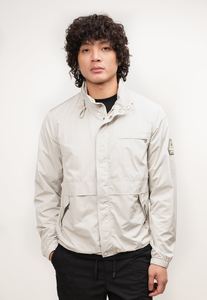 Mens lightweight stone windbreaker modeled by a man with curly hair, showcasing its stylish design and features.