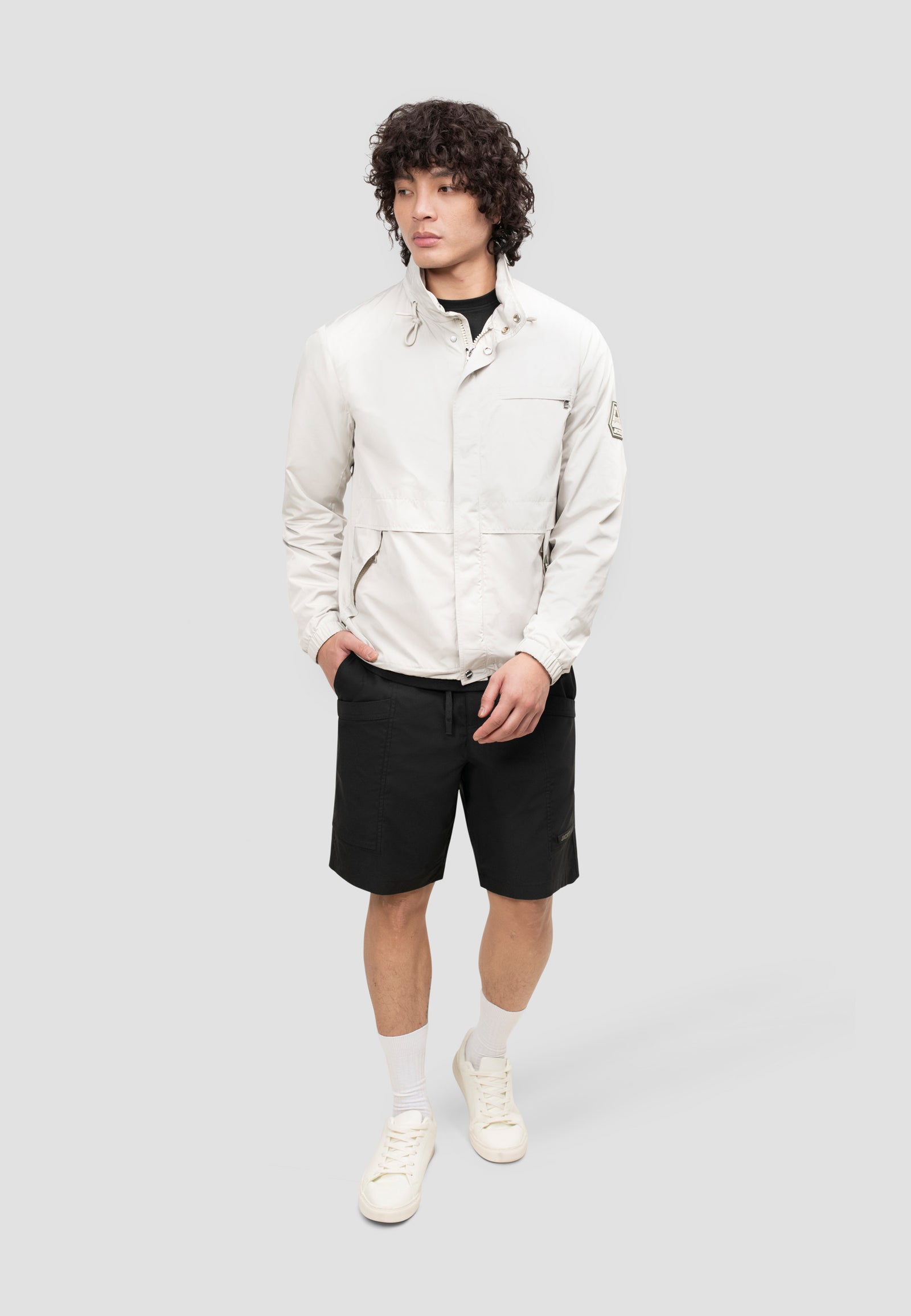 Men's stone windbreaker model wearing lightweight jacket with shorts for spring and summer style.