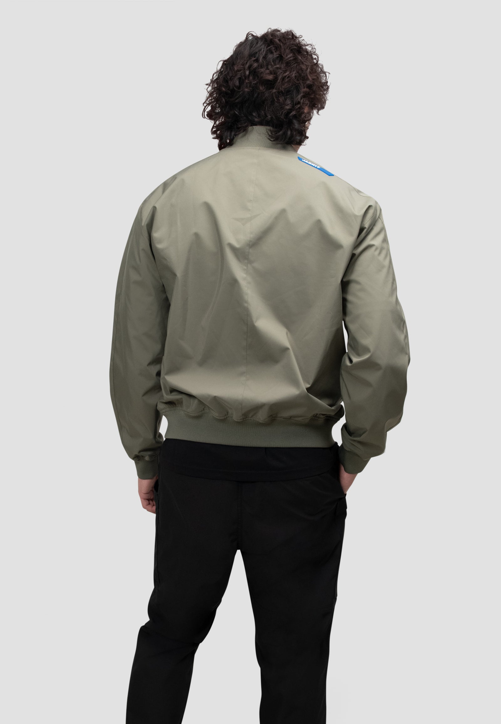 Back view of a model wearing a mens olive bomber jacket in dusty olive color.