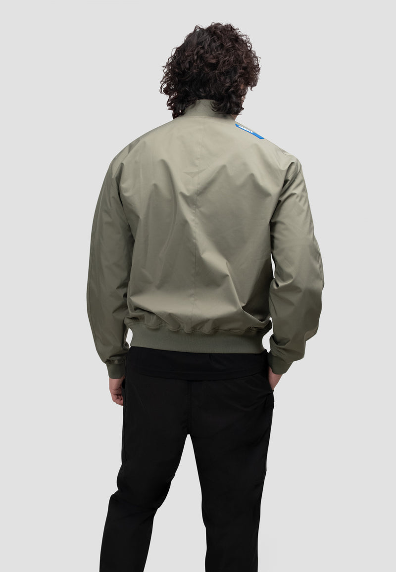 Back view of a model wearing a mens olive bomber jacket in dusty olive color.