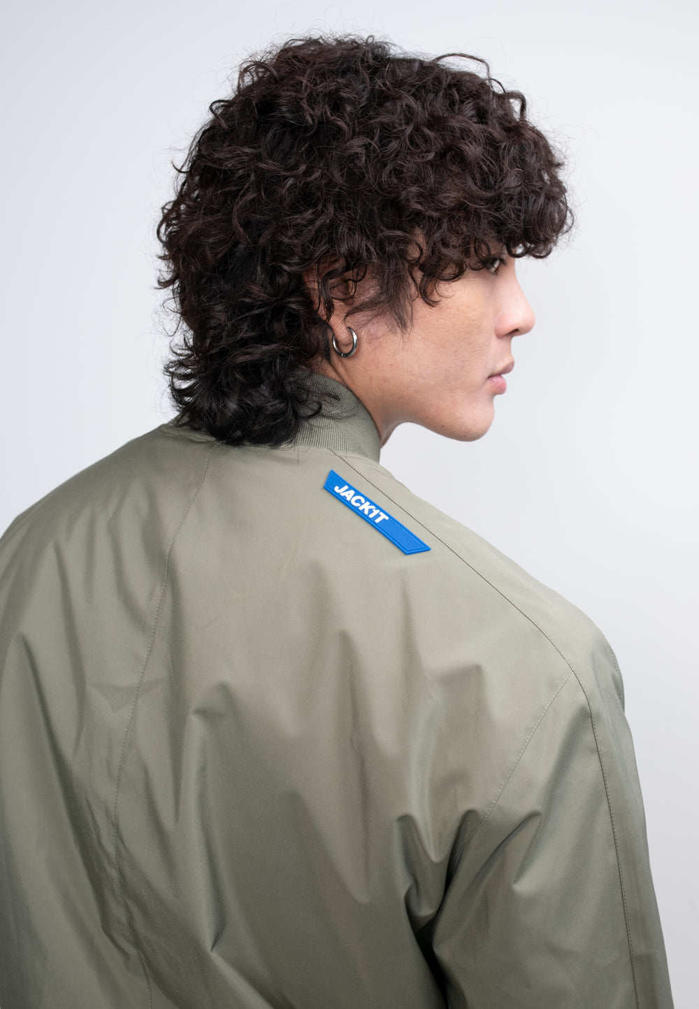 Model wearing mens olive bomber jacket, showcasing the back design and modern detail in lightweight fabric.