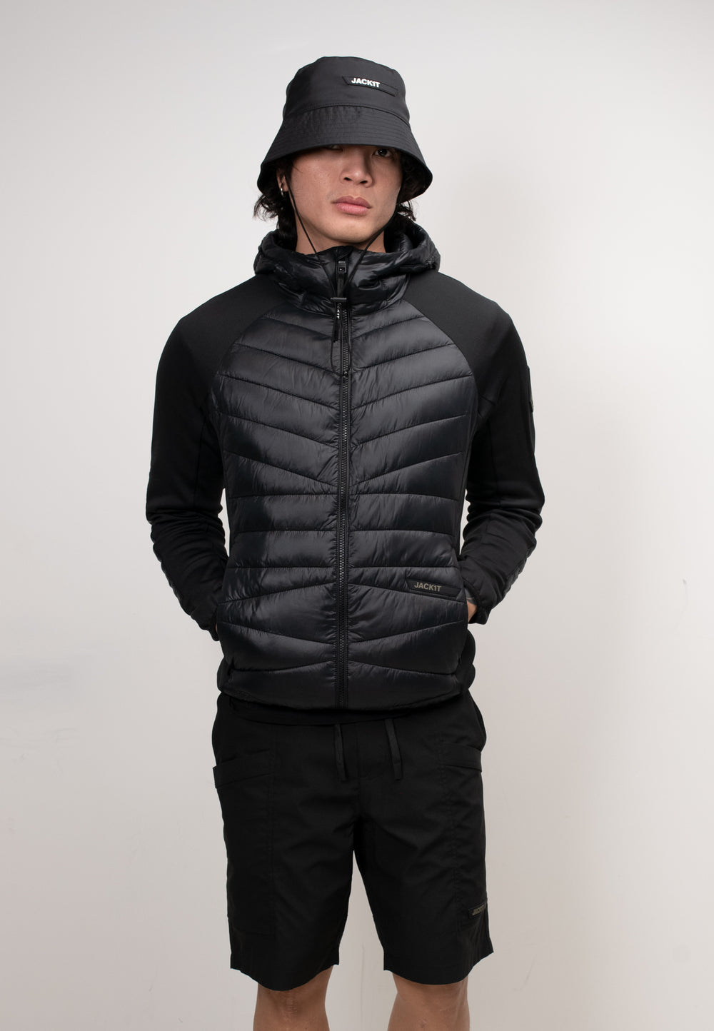 Men's black hooded jacket styled with shorts and a bucket hat, showcasing a lightweight design and THERMOLITE® insulation.