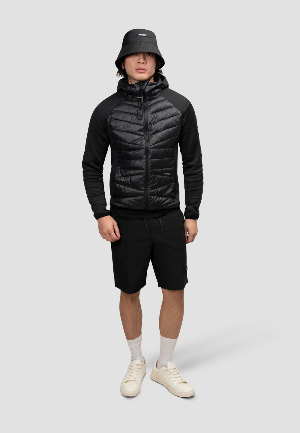 A model wearing a men's black hooded jacket paired with shorts and a bucket hat.