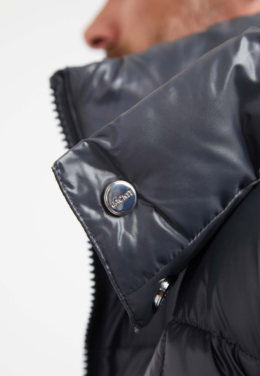 Close-up of the collar on a mens grey racer jacket, showcasing the shiny fabric and metal snap detail.