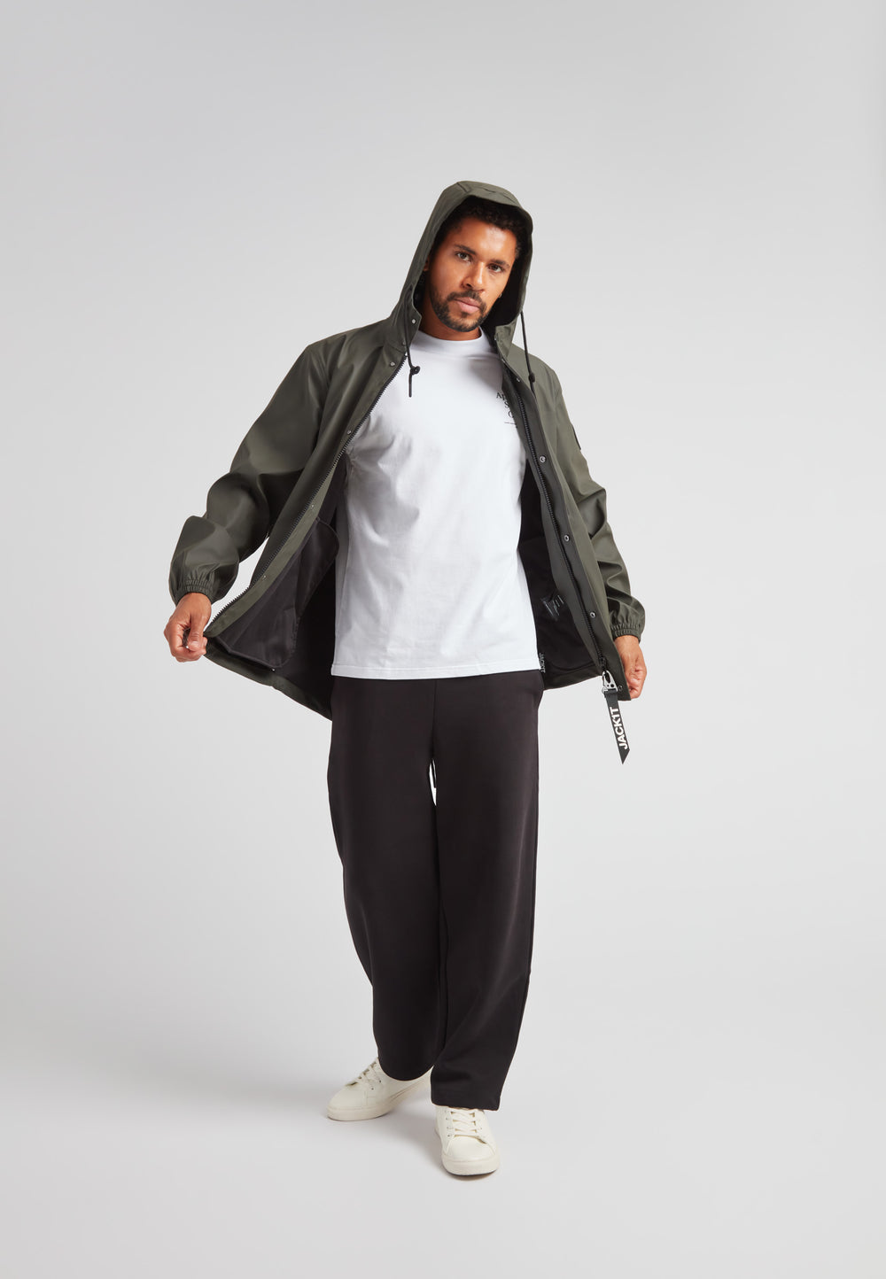 Man wearing ELEMENTS Unisex Raincoat 2.0 Khaki with a hood, styled with a white t-shirt and black pants.