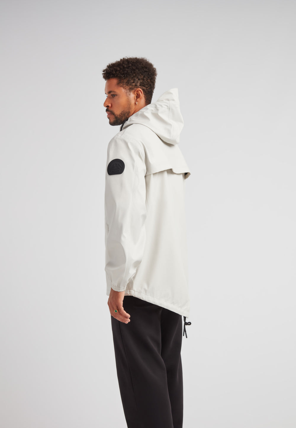 Side view of man wearing ELEMENTS Unisex Raincoat 2.0 Stone with hood and stylish design.