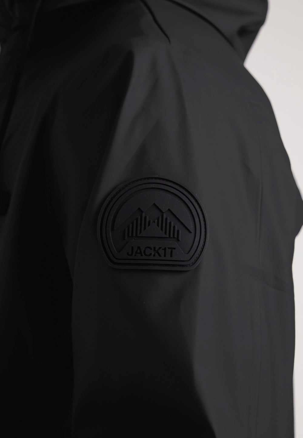 Close-up of JACK1T logo on sleeve of ELEMENTS Unisex Raincoat 2.0 Black, showcasing its sleek design.