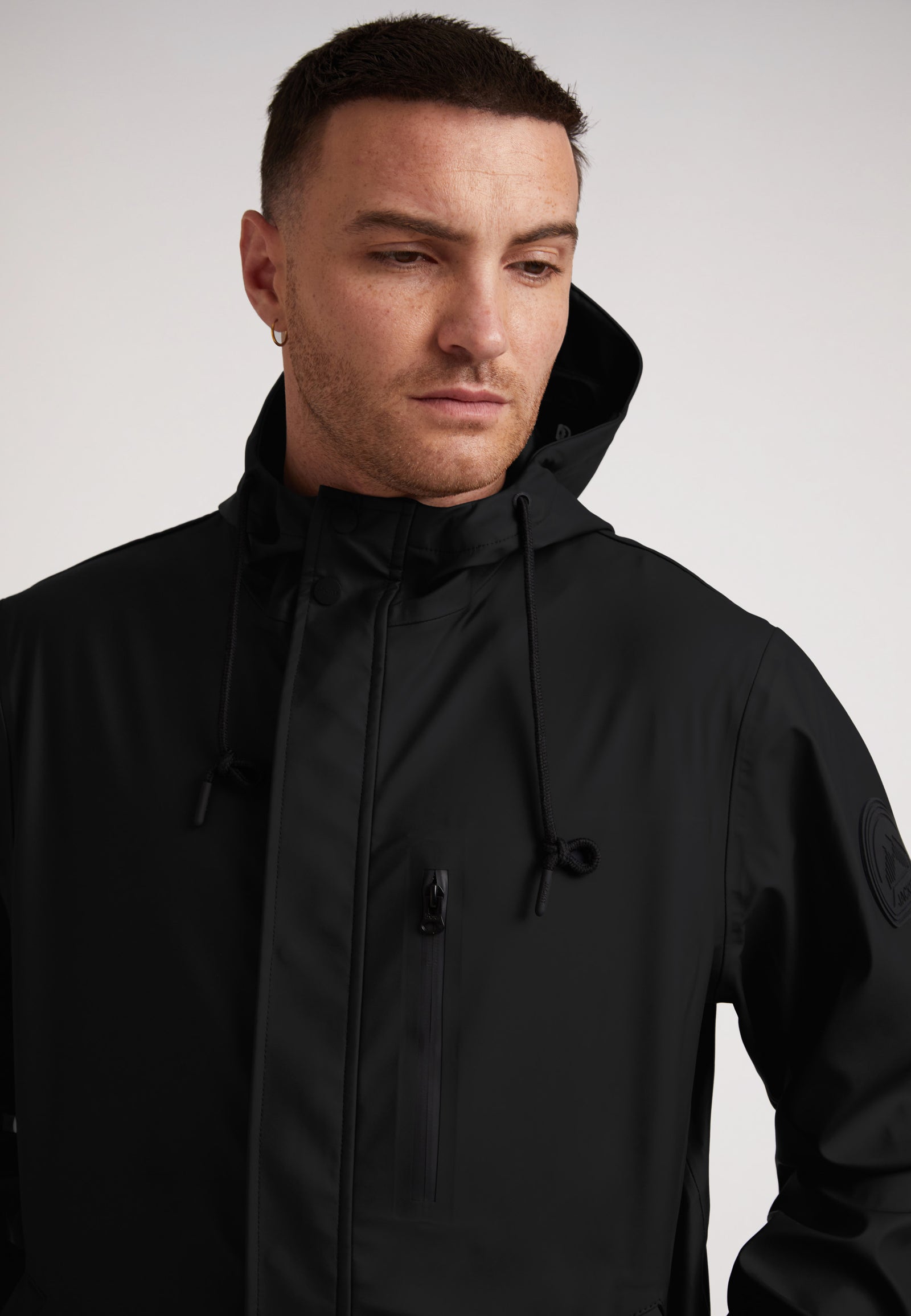 Close-up of a man wearing the ELEMENTS Unisex Raincoat 2.0 Black against a neutral background.