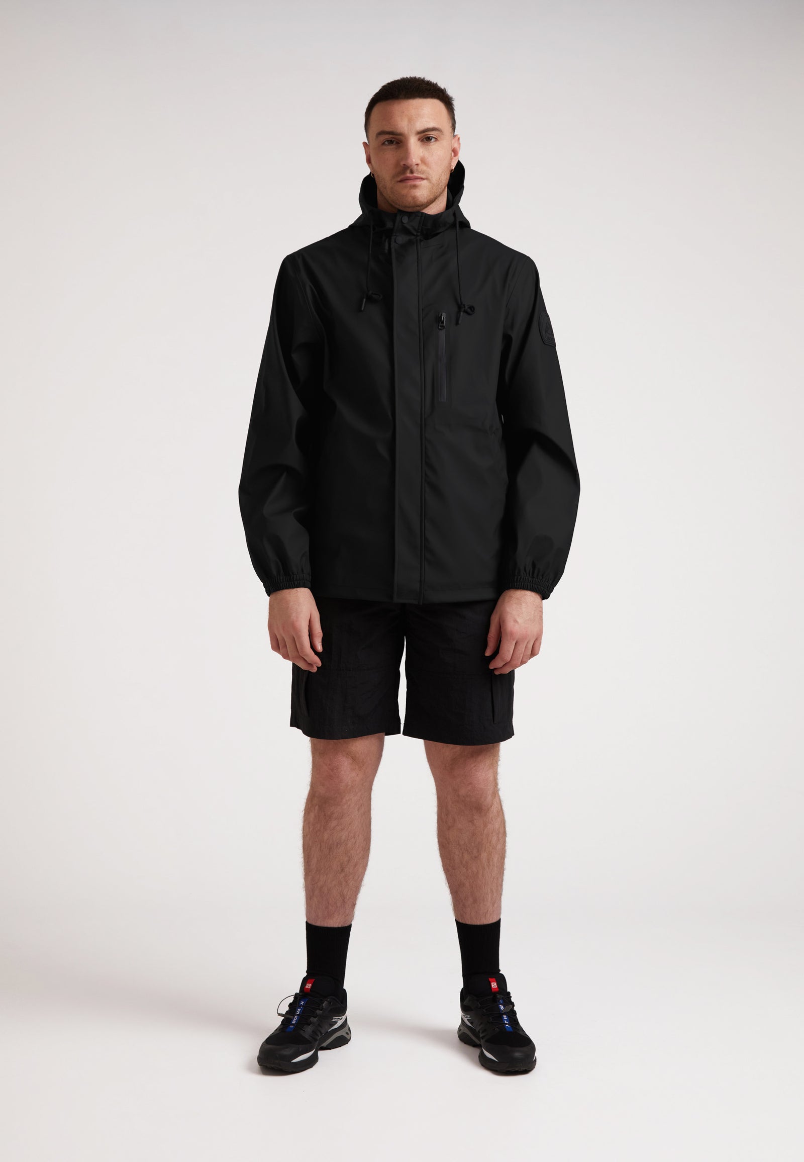 Model wearing ELEMENTS Unisex Raincoat 2.0 Black with shorts and sneakers.