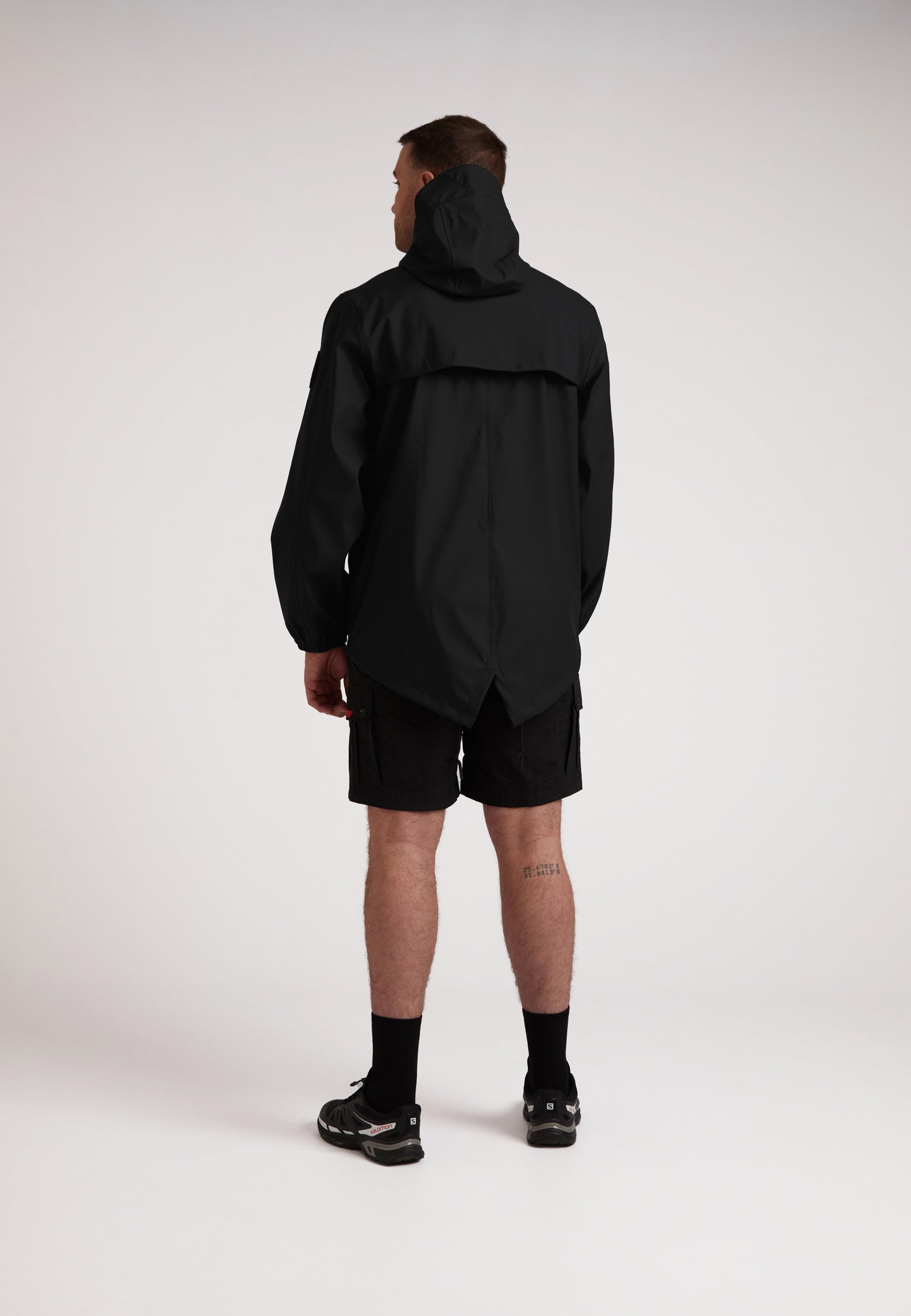 Back view of a model wearing the ELEMENTS Unisex Raincoat 2.0 Black with shorts, showcasing its lightweight design.