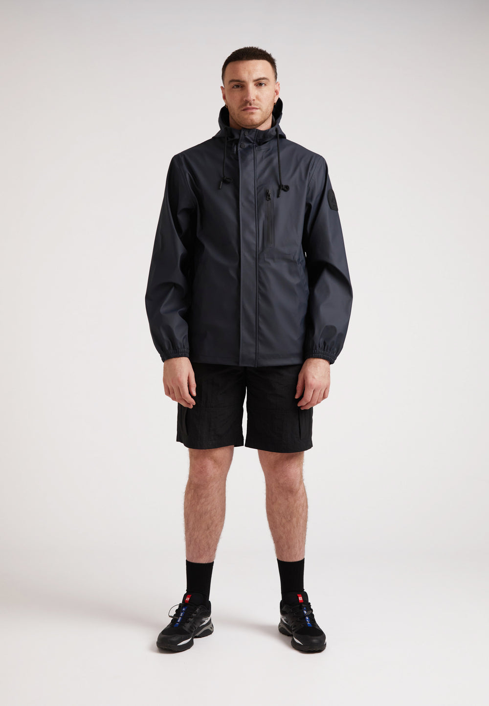 A model wearing the ELEMENTS Unisex Raincoat 2.0 Navy with shorts, showcasing versatile weather protection.