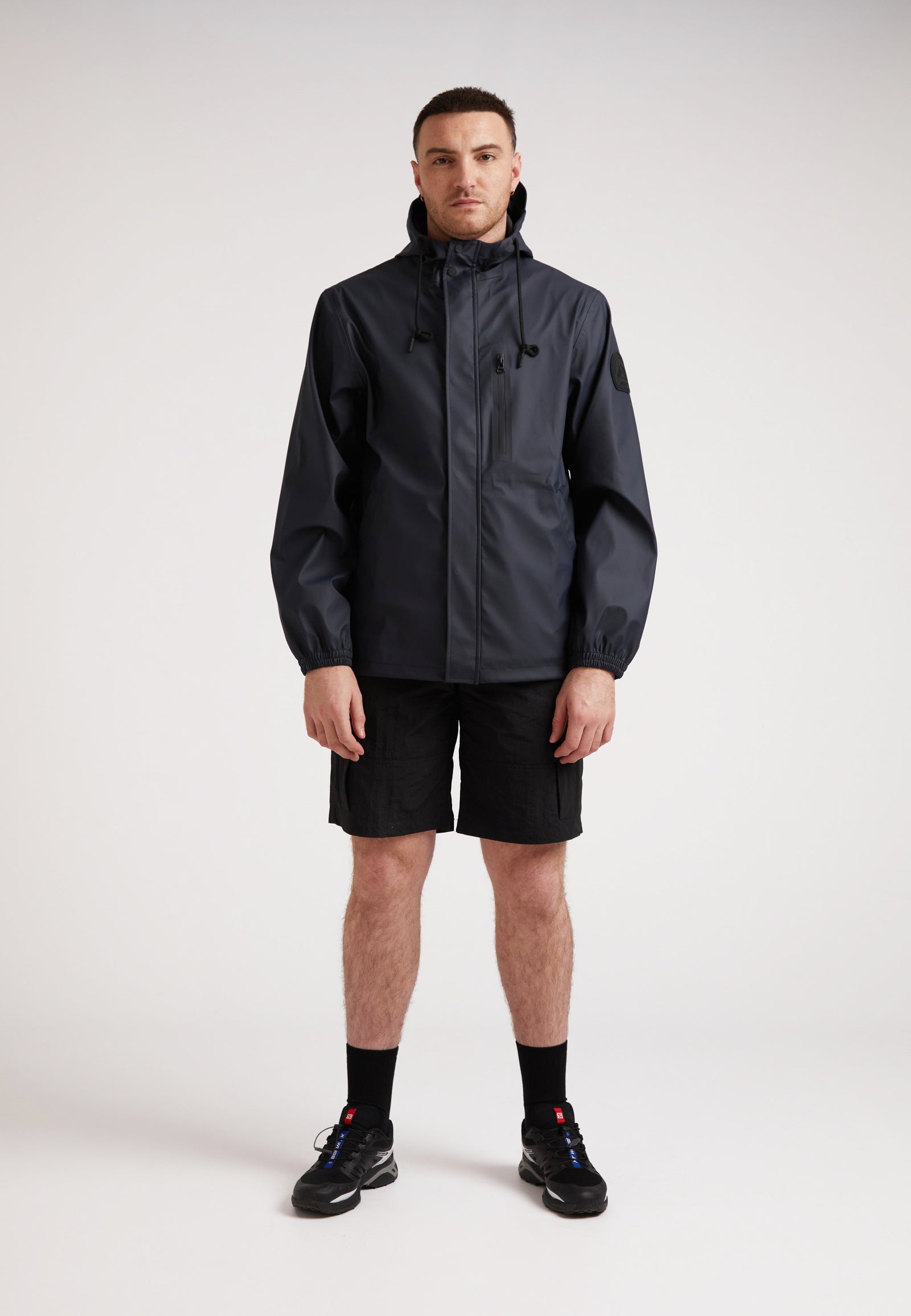A model wearing the ELEMENTS Unisex Raincoat 2.0 Navy with shorts, showcasing versatile weather protection.