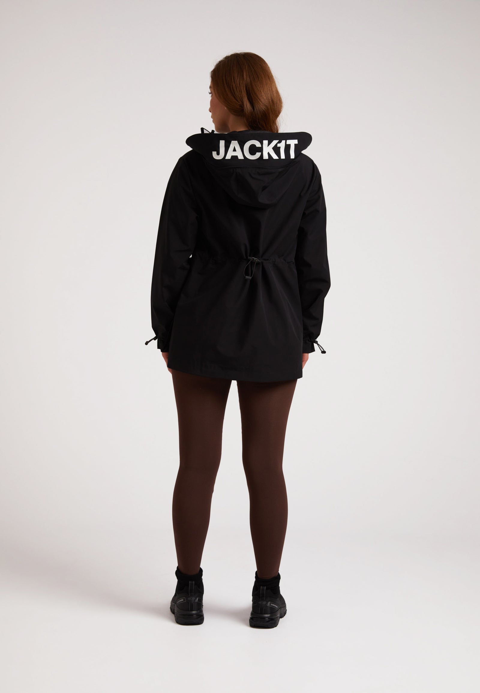 Back view of a person wearing HELIO Mid Windbreaker Black with JACKIT branding on the hood.