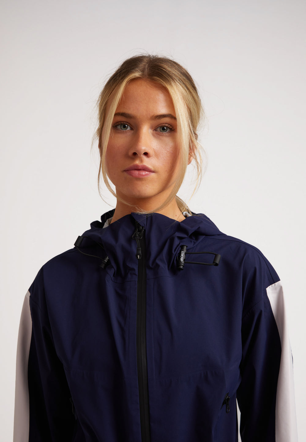 Model wearing a Ladies waterproof lightweight navy jacket with adjustable hood and zippers.