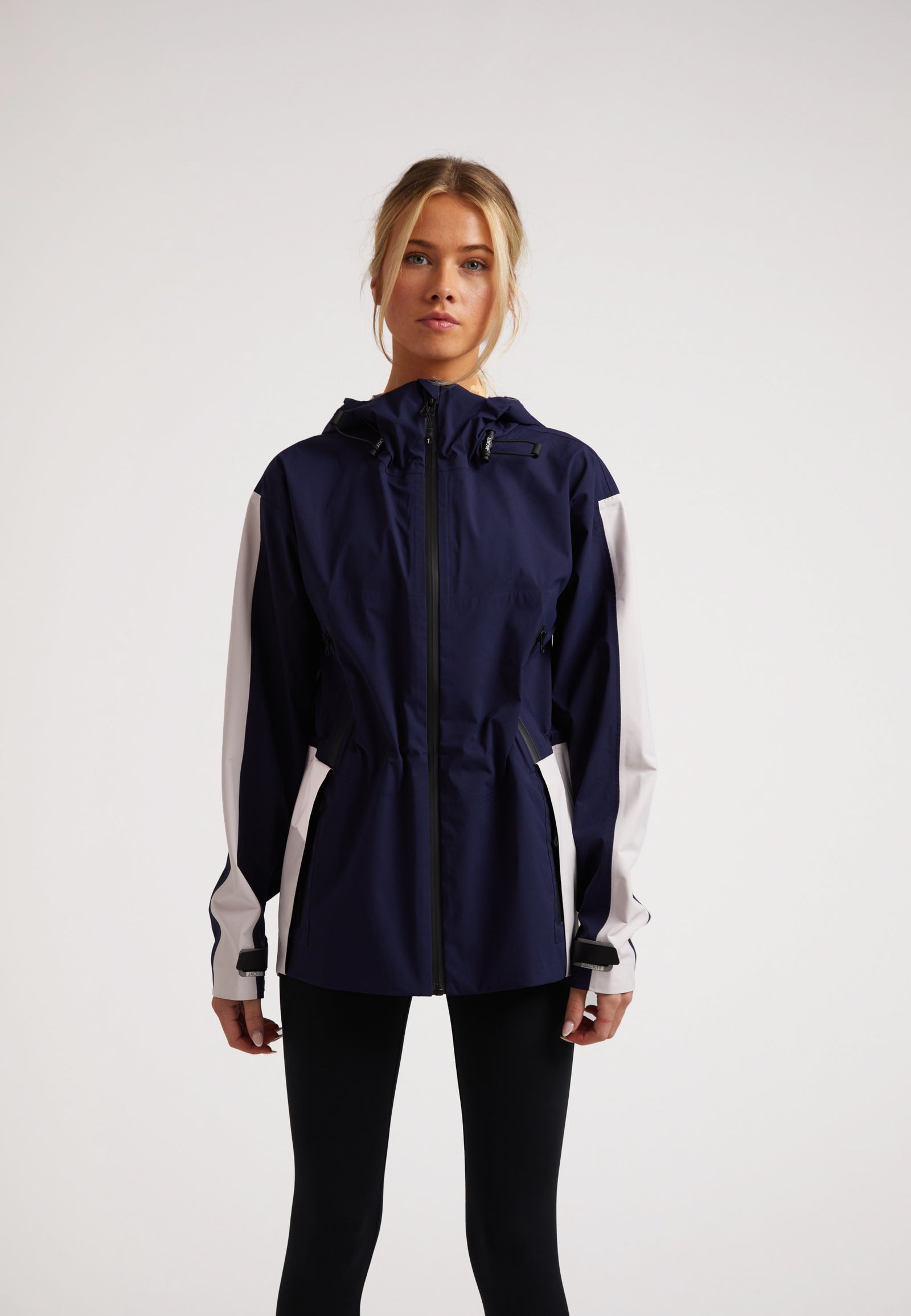 Model wearing a Ladies waterproof lightweight navy jacket with adjustable hood and cuffs, designed for performance in various weather.