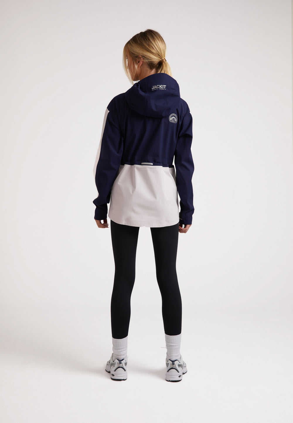 Model wearing a ladies waterproof lightweight navy jacket with adjustable hood and taped seams.