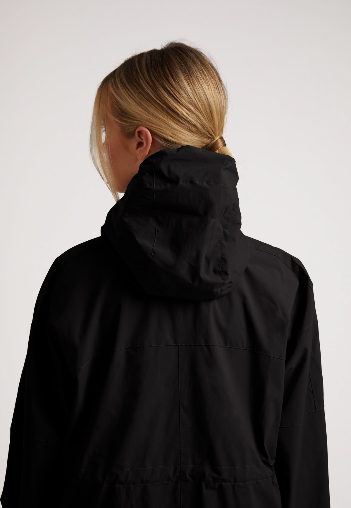 Back view of a woman wearing the ISOTOPE Ladies lightweight black windbreaker with a hood.
