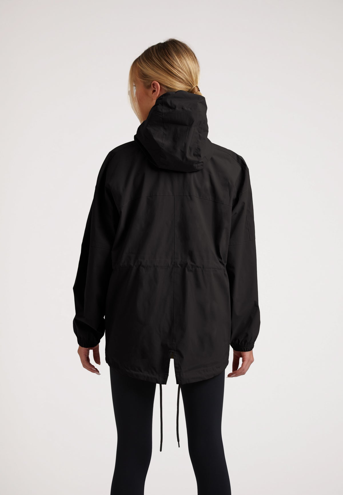 Back view of model wearing the ISOTOPE Ladies lightweight black windbreaker with hood and adjustable hem.