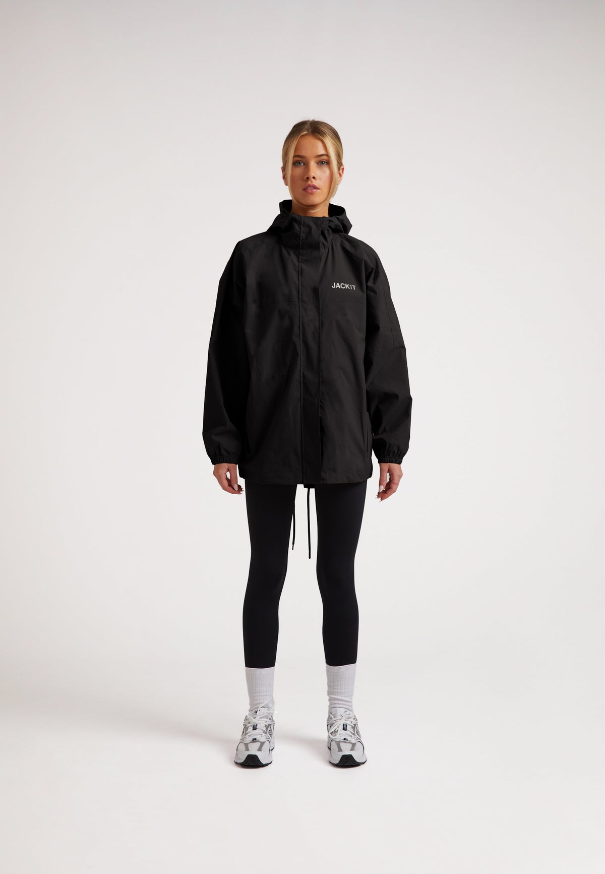 Model wearing ISOTOPE Ladies lightweight black windbreaker, featuring a hood and reflective elements.