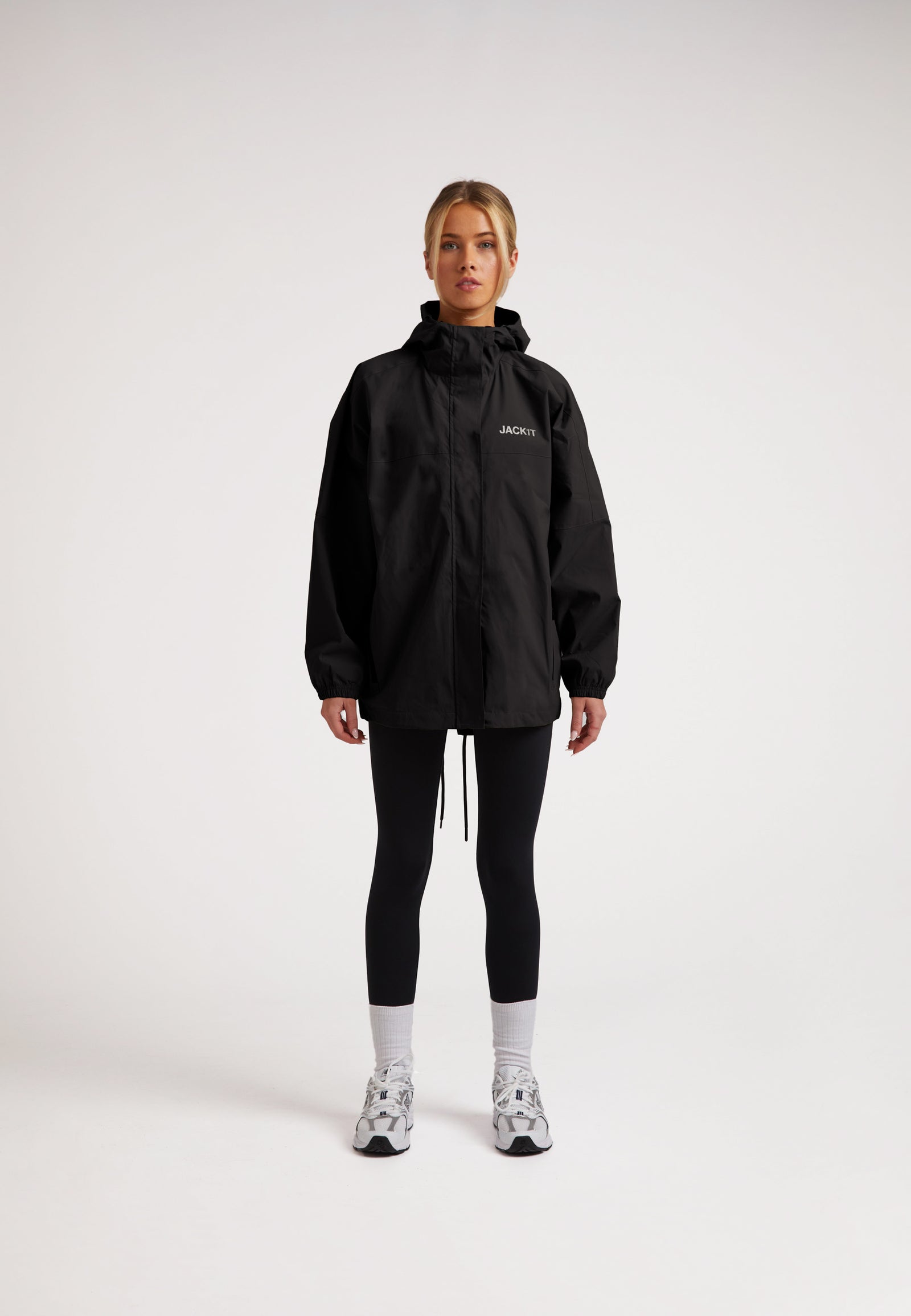 Model wearing ISOTOPE Ladies lightweight black windbreaker, featuring a hood and reflective elements.