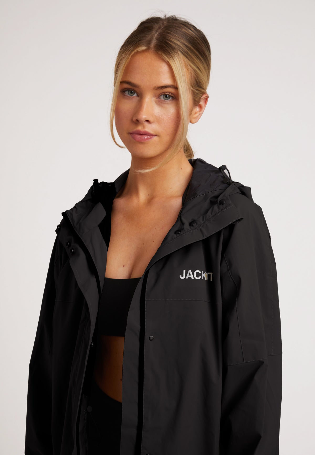 Model wearing ISOTOPE Ladies lightweight black windbreaker with hood and reflective details.