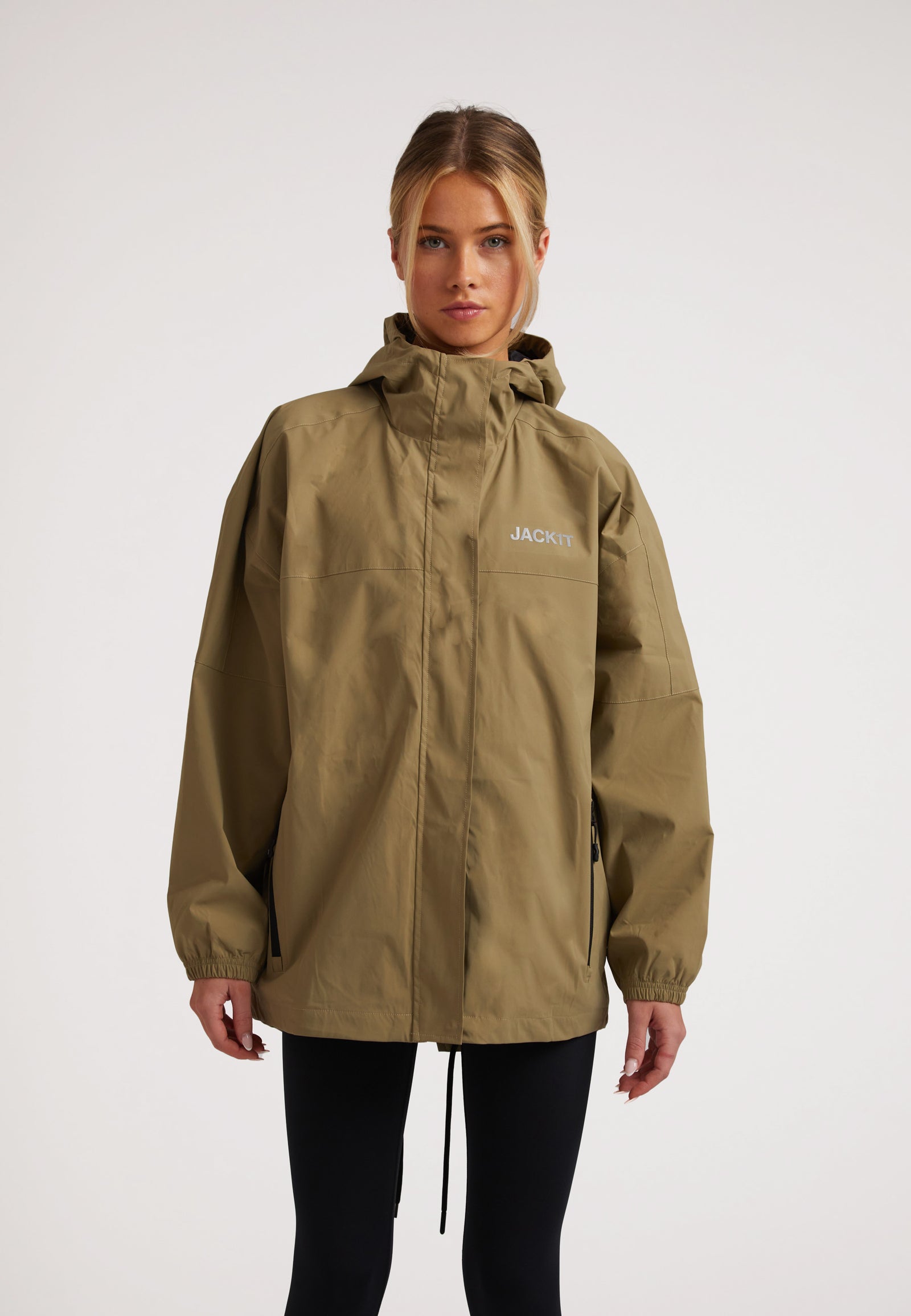 Model wearing the ISOTOPE Ladies lightweight olive windbreaker with hood and zip pockets, showcasing a stylish casual look.