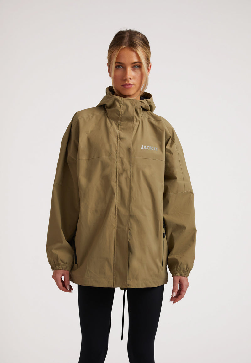 Model wearing the ISOTOPE Ladies lightweight olive windbreaker with hood and zip pockets, showcasing a stylish casual look.