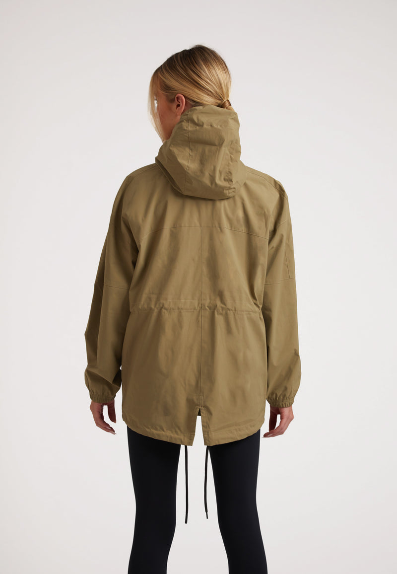 Rear view of a model wearing Ladies lightweight olive windbreaker with hood and drawstring hem