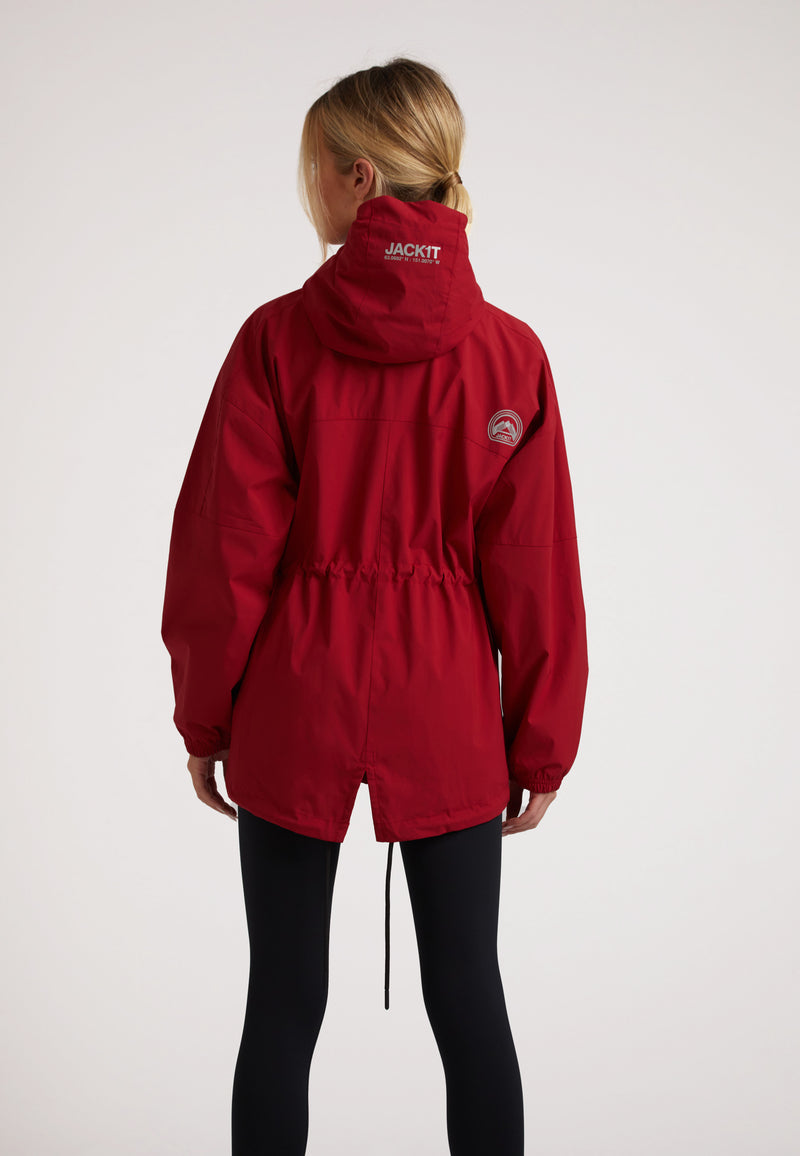 Back view of a model wearing a Ladies red lightweight windbreaker with adjustable hem and hood.