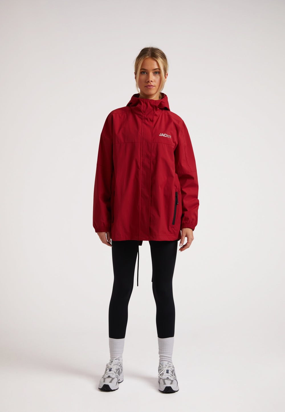 Model wearing ISOTOPE Ladies red lightweight windbreaker, featuring a hood and pockets, styled with black leggings.