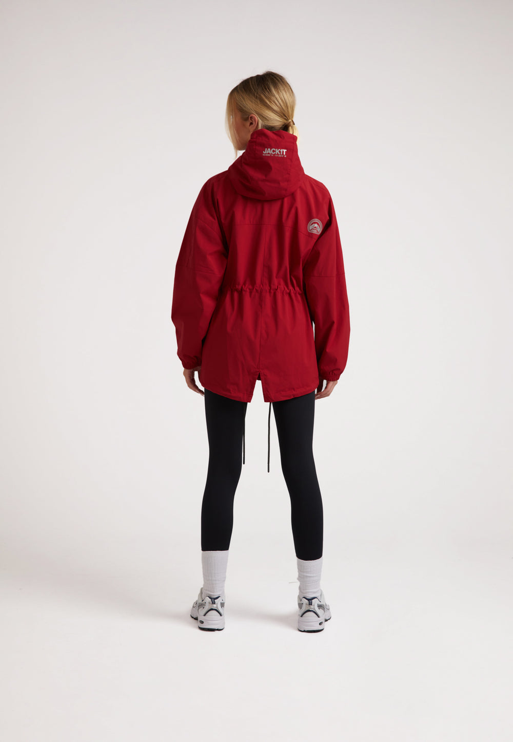 Back view of a model wearing a ladies red lightweight windbreaker with a drawstring waist.