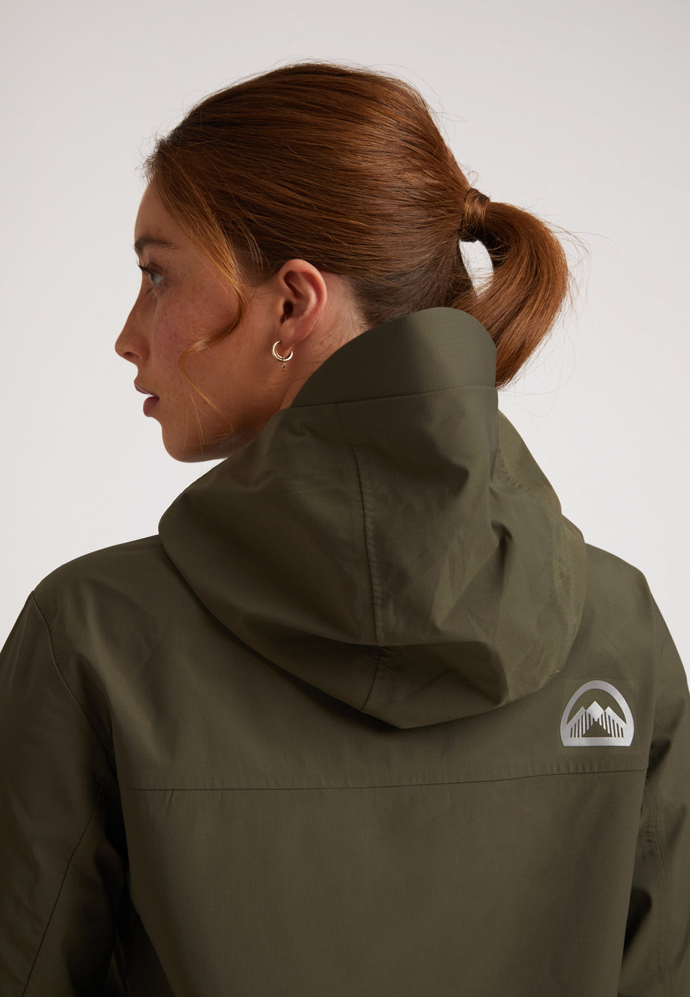 Back view of a woman wearing the LITHIUM Waterproof ladies jacket in olive with a hood.