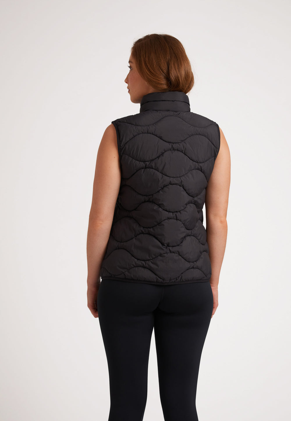 Woman wearing ORB1T Quilted Gilet Black, showcasing its onion baffle design from the back view.