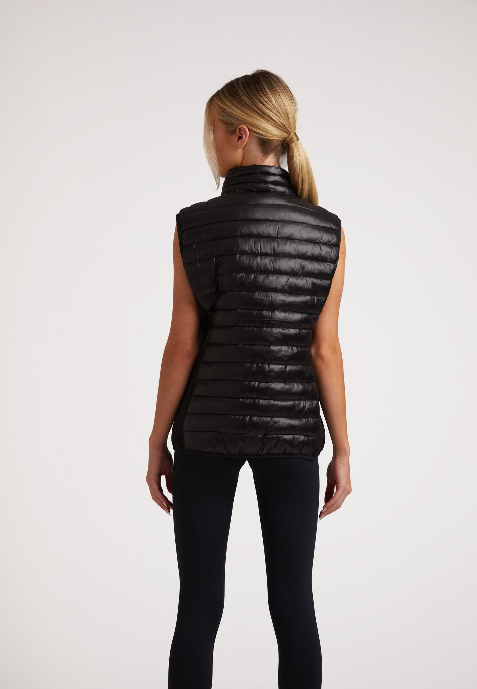 Back view of a woman wearing the SPORTL1TE Funnel Lightweight Gilet 2.0 Lux Black, showcasing its sleek design and lightweight fabric.