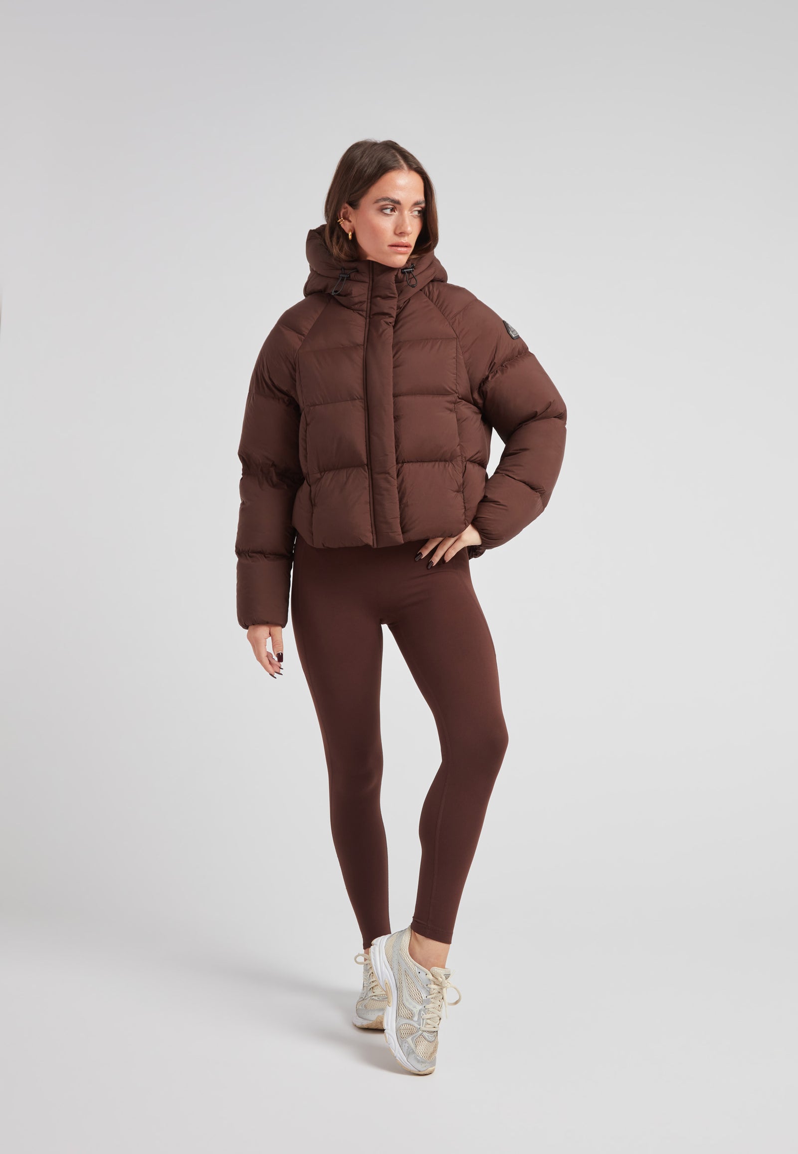 Ladies Cloud Crop Down Puffer Jacket in Mid Brown worn with leggings and sneakers, showcasing its stylish design.