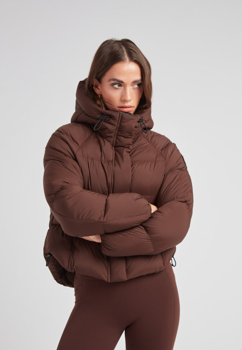 Ladies Cloud Crop Down Puffer Jacket in Mid Brown worn by a model, showcasing a stylish cropped design and oversized hood.