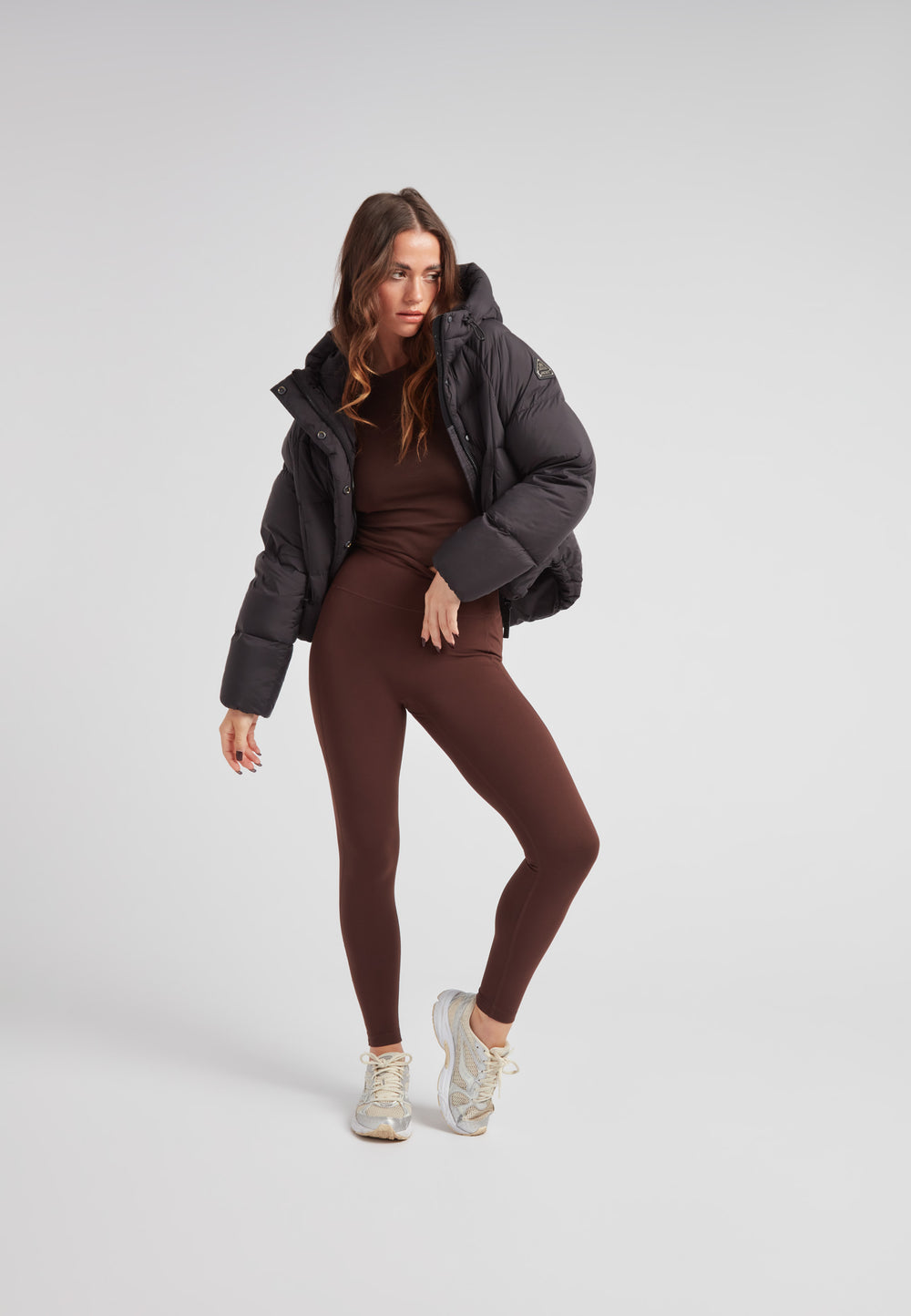 Model wearing the Cloud Crop Down Puffer Jacket Black with brown leggings and sneakers, showcasing stylish winter fashion.