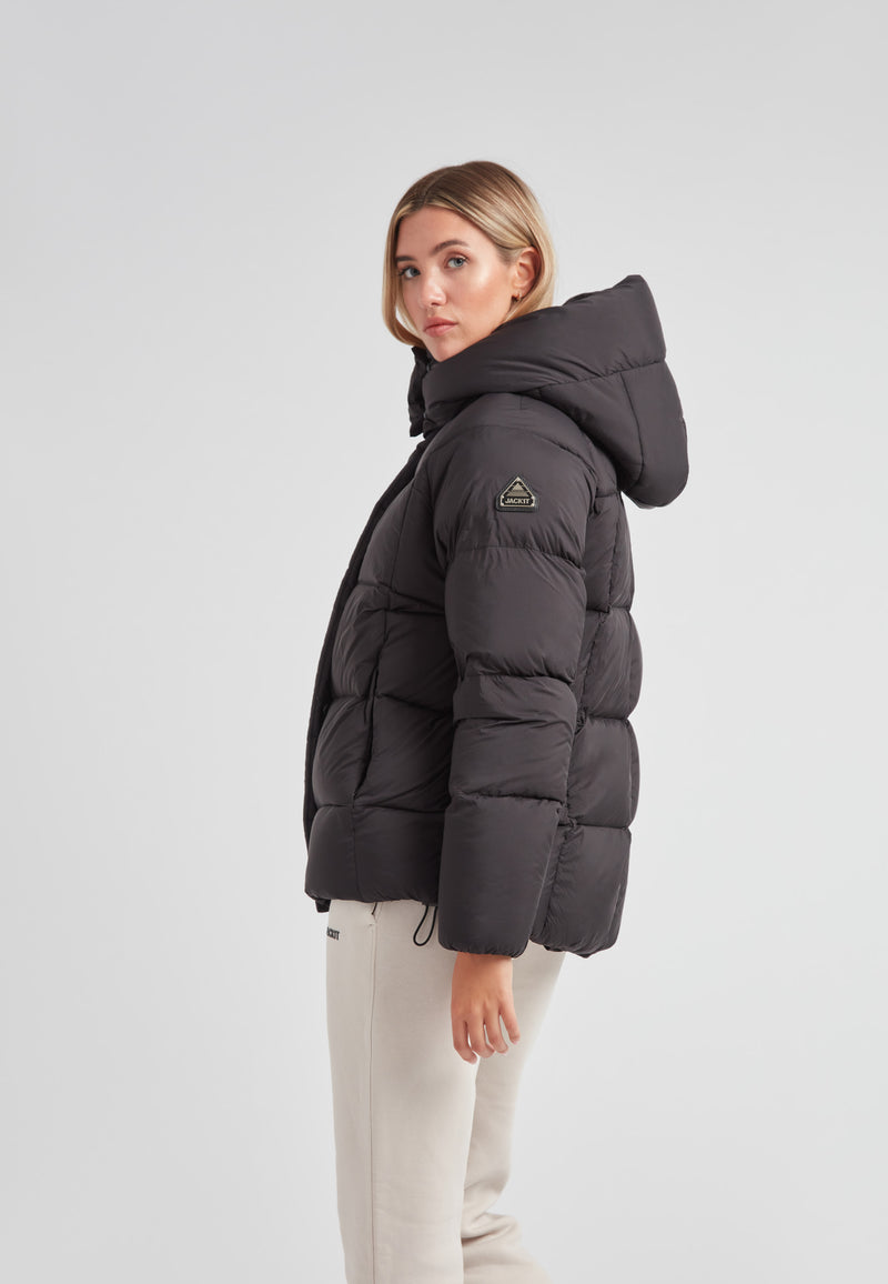 Cloud Prime Longline Down Puffer Jacket Black worn by a woman, showcasing its stylish design and adjustable hood.