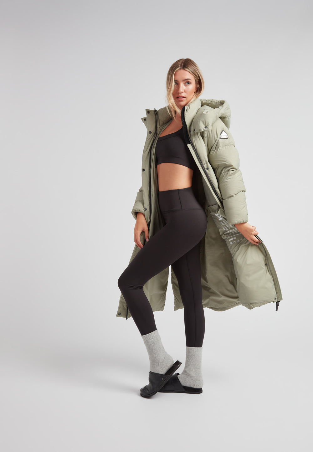 Model wearing a Cloud Ultra Long Down Puffer Coat in olive green with black activewear and socks.
