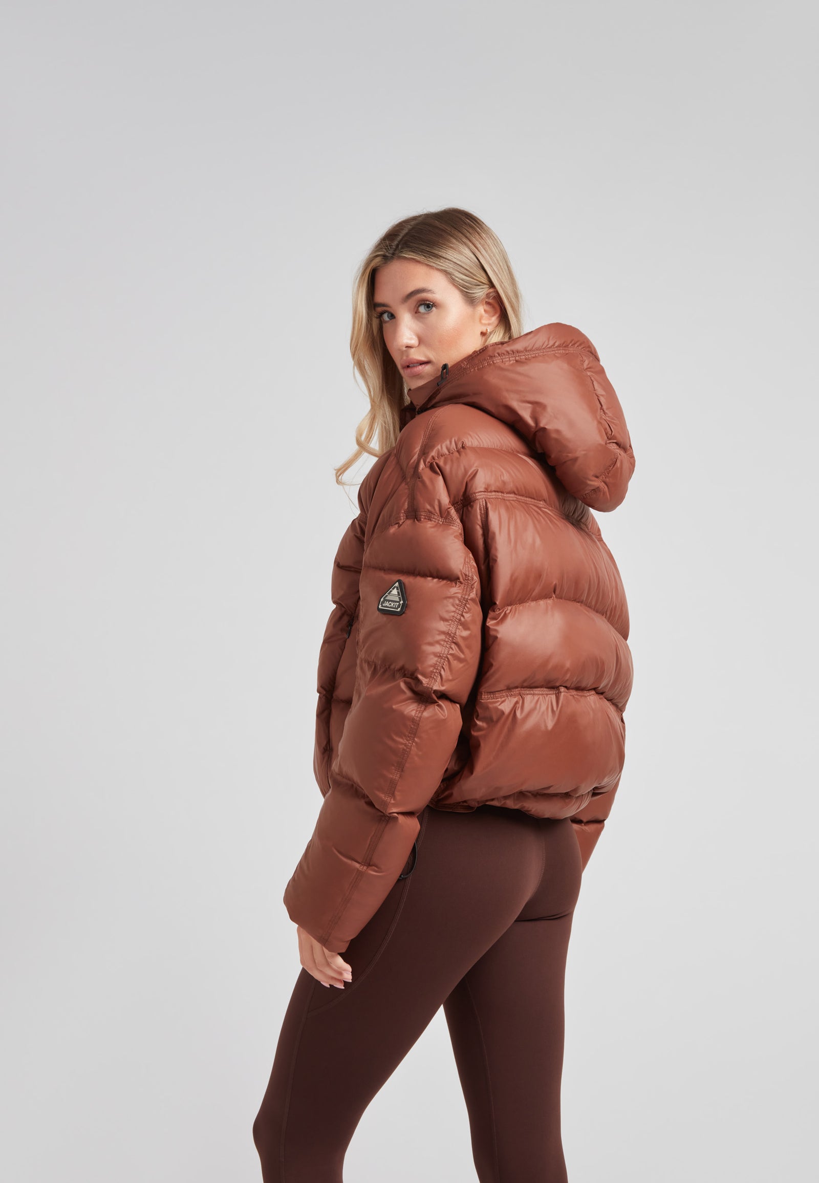 Cropped puffer in mocha brown with adjustable coverage, showcasing the stylish drop-shoulder design and hood.
