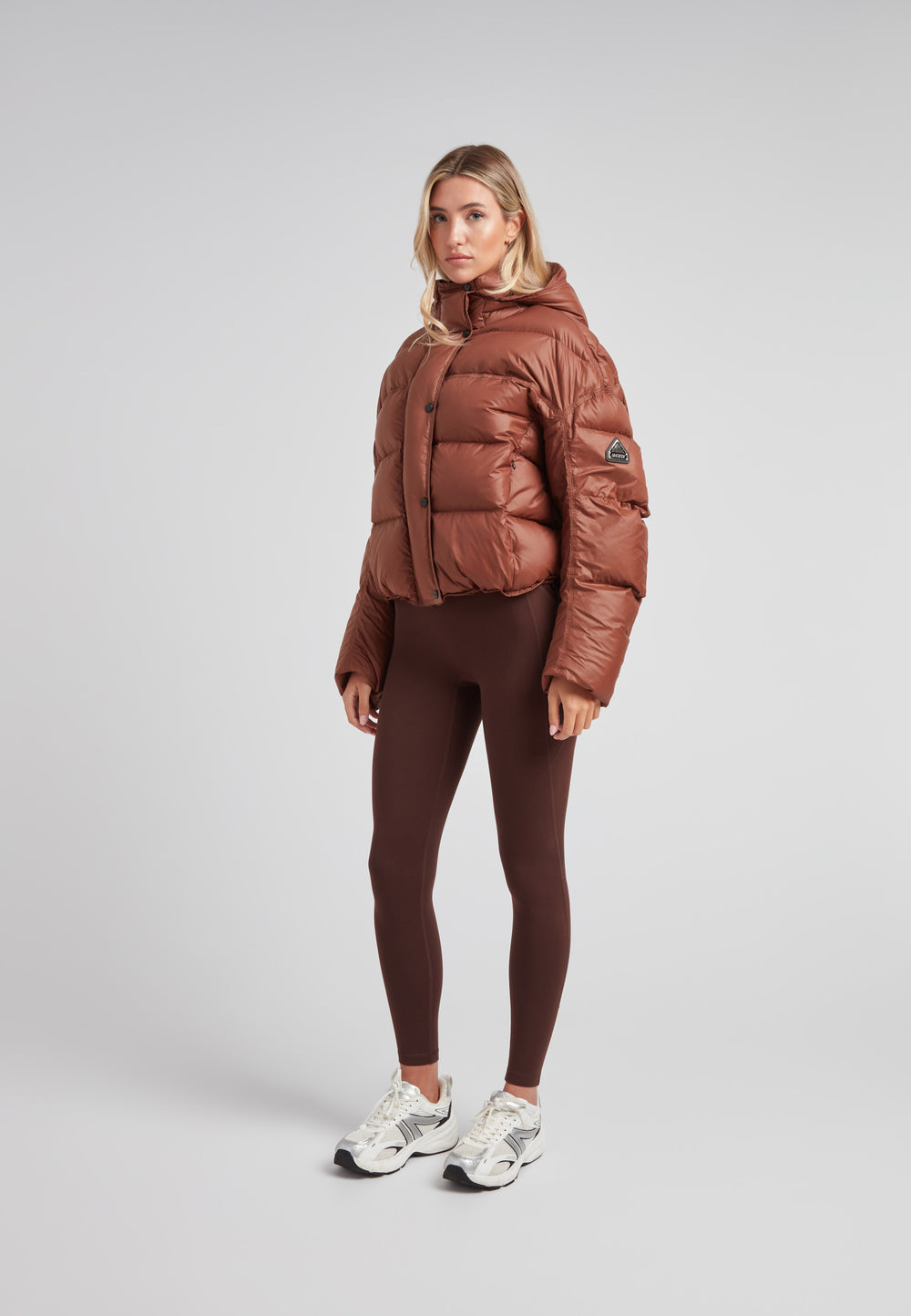 Cropped puffer in mocha brown with adjustable coverage worn by a model, showcasing its oversized design and drop-shoulder silhouette.