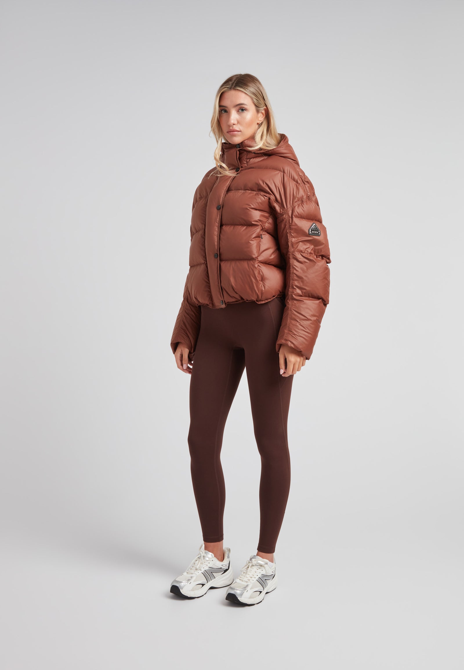 Cropped puffer in mocha brown with adjustable coverage worn by a model, showcasing its oversized design and drop-shoulder silhouette.